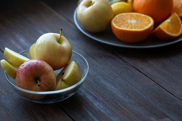 apples in a plate next to other fruits on a black wooden table