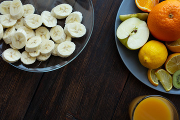 banana slices in a plate on a dark wooden background next to other fruits and a glass of juice