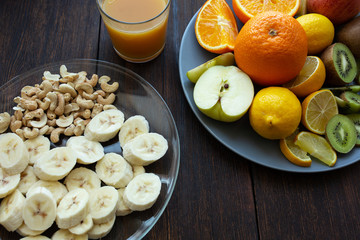 banana slices in a plate on a dark wooden background next to other fruits and a glass of juice