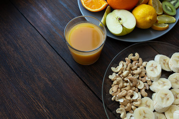 banana and cashew slices in a plate on a dark wooden background next to other fruits and a glass of juice