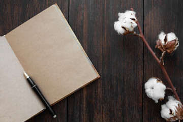 craft notebook with pen and cotton branch on a dark wooden background top view