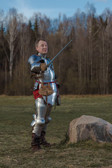 A knight on foot in armor and holding a sword in his hands shows combat attacks on the battlefield.
