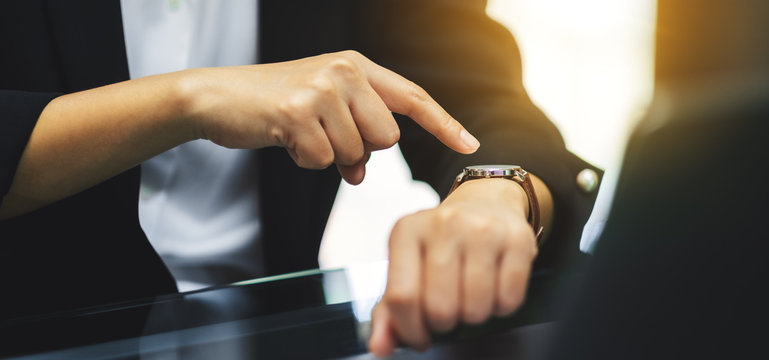 A business woman pointing at a wristwatch on her working time while waiting for someone in office