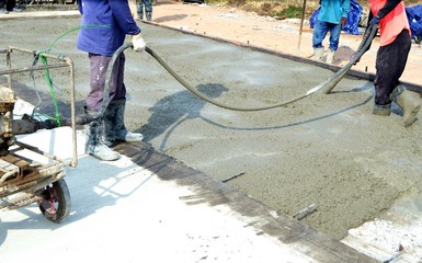 Construction workers using concrete vibrator for concrete density at road pavement construction site.