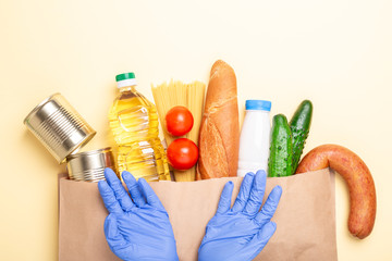 Donation paper bag with food stock and hands in and medical gloves. Delivery service, coronavirus covid-19. Top view