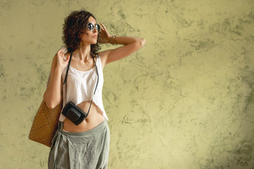 Obraz premium A girl with sunglasses and a camera against the wall. The concept of travel. Copy space