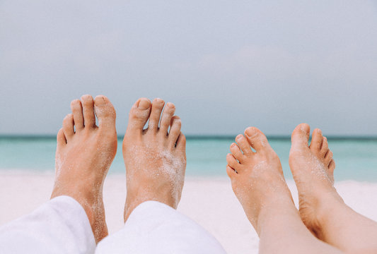 Male's and woman's legs on the white sand near the sea.