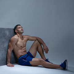 serious handsome male in stylish without  t shirt, looks aside, thinks about something, poses over grey wall. Space for text.