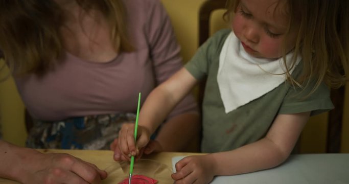Preschooler mixing paint with his mother to use on a piece of paper