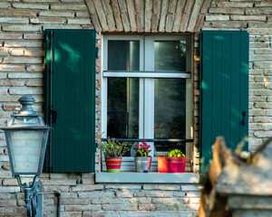 Una finestra con fiori sul davanzale con riflesso del cielo e bei colori, con una lanterna di fianco © Mattia Golinucci