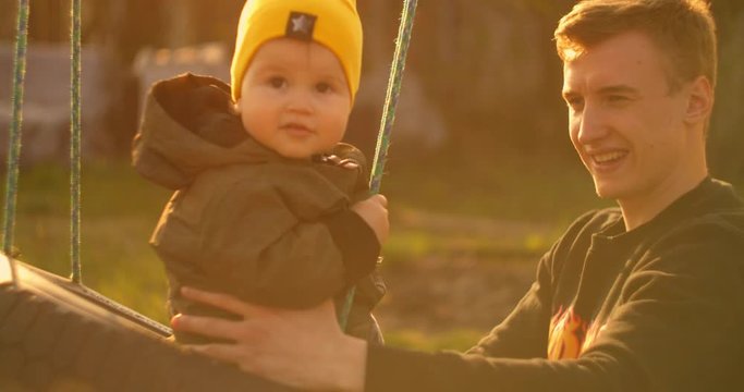 Happy dad rolls a cheerful son on a swing in a park on an oak tree. The concept of a happy family. Single father. Slow motion father and son on a swing on father day.
