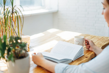 Friendly charming brunette woman reading book at table in the bright interior