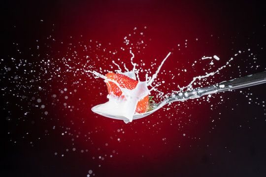A tasty ripe red Strawberry fall into milk in front of a gradient red backdrop on a tablespoon and are splashed - Strawberry Splash
