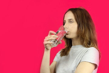 girl with long hair drinks water on a pink background, copy space