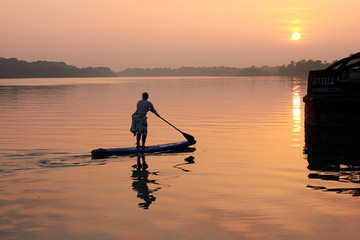 Silhouette of fat middle-aged woman on Stand Up Paddle Board at sunset in Danube river. SUP.