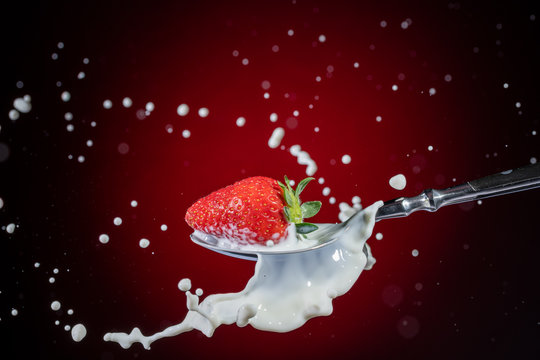 A tasty ripe red Strawberry fall into milk in front of a gradient red backdrop on a tablespoon and are splashed - Strawberry Splash