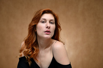Naklejka premium Model posing without makeup. Close-up portrait of a young pretty woman with long red hair on a beige background.