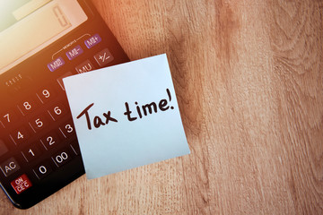 Tax time on blue note sticker with calculator and pen on wooden background