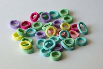  multi-colored elastic bands round for fixing hair pink, yellow, green randomly scattered on a white surface selective focus