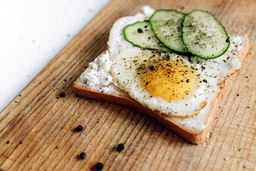Toast with fried egg and fresh cucumber on a wooden stand. Delicious quick breakfast