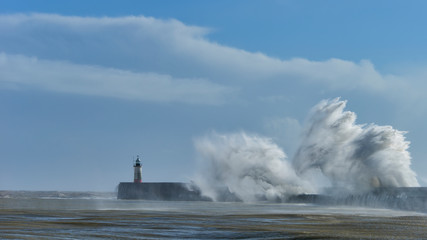 Naklejka na ściany i meble Massive waves crash over harbour wall onto lighthouse during huge storm on English coastline in Newhaven, amazing images showing power of the ocean