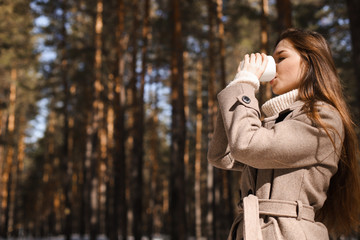 Beautiful girl drinks hot tea, hot chocolate, coffee in a warm spring forest. The concept of spring warmth, atmosphere and comfort. With place for an inscription.