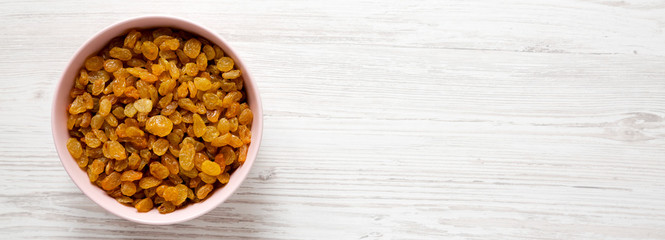 Golden Raisins in a Pink Bowl on a white wooden surface, top view. Flat lay, overhead, from above. Space for text.