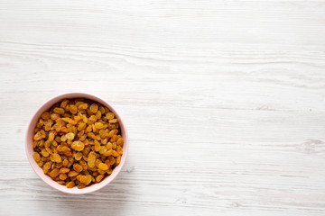 Golden Raisins in a Pink Bowl on a white wooden background, top view. Flat lay, overhead, from above. Copy space.