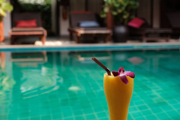 Fototapeta na wymiar Mango smoothie in a tall glass on the background of the pool