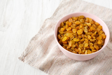 Golden Raisins in a Pink Bowl on a white wooden background, side view. Copy space.