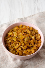 Golden Raisins in a Pink Bowl on a white wooden background, low angle view. Copy space.