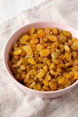 Golden Raisins in a Pink Bowl on a white wooden surface, low angle view. Close-up.