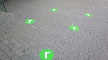 Social distancing: green markers for people at the bus stop to avoid contact and infection. Coronavirus and Covid 19 time frame. Empty area. Grey bricks