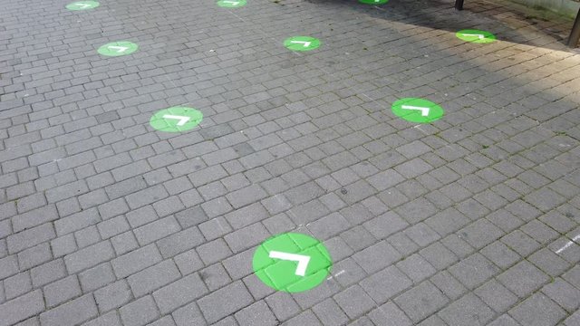 Social distancing: green markers for people at the bus stop to avoid contact and infection. Coronavirus and Covid 19 time frame. Empty area. Grey bricks