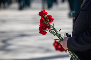 A hand puts red carnations on a granite gravestone. Memory of the dead