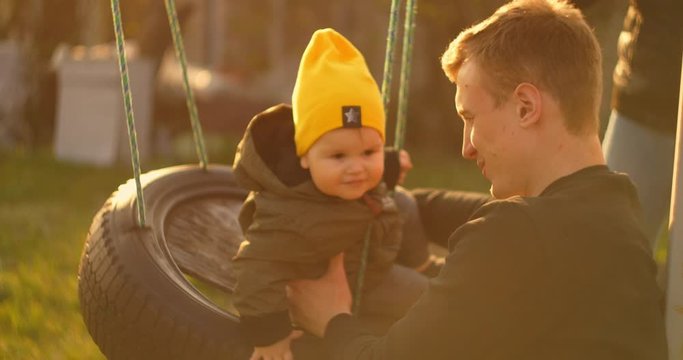 Happy dad rolls a cheerful son on a swing in a park on an oak tree. The concept of a happy family. Single father. Slow motion father and son on a swing on father day.