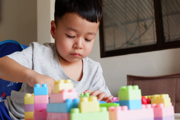 Close up of child's hands playing with colorful plastic bricks at the table. Toddler having fun and building out of bright constructor bricks. Early learning. stripe background. Developing toys