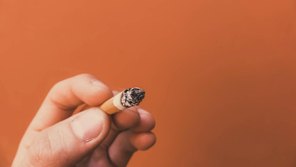 smoldering cigarette in his hand on an orange background