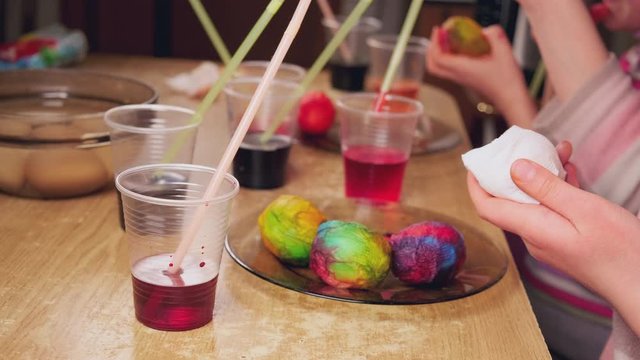Close up video of hands of children using dye and painting on white boiled eggs while preparing for Easter, 4K UHD video