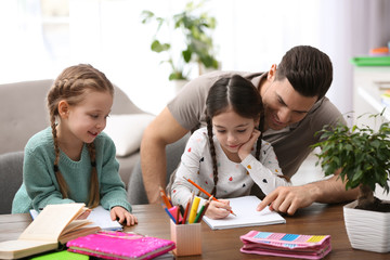 Father helping his daughters with homework at table indoors