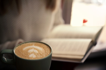 Woman with coffee reading book indoors, focus on cup