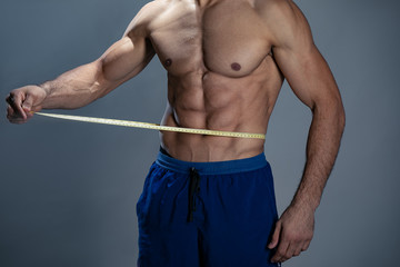 Muscular fitness man measuring his waist - studio shoot