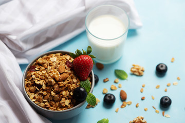 A bowl, a cup with freshly prepared granola is on a blue table next to a glass of milk. Homemade...