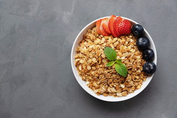 A ceramic bowl with homemade granola stands on a dark background. Muesli with fresh berries. Place for text. Homemade breakfast, snack. Proper diet