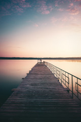 Obraz premium Drewniany most nad jeziorem. Rybak na moście o zachodzie słońca. Spokojne miejsce. Jezioro o zachodzie słońca