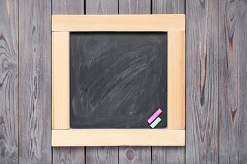 Blackboard with pieces of color chalk on wooden background, top view. Space for text