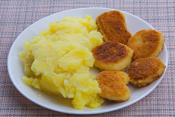 Boiled mashed potatoes on a plate with chicken nuggets on table