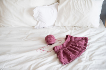 on a white bed lies a children's knitted skirt, next to it is a skein of thread