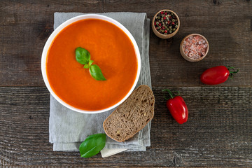 Vegetarian lunch meal tomato cream soup with fresh basil and bread on the old wooden table. Top view