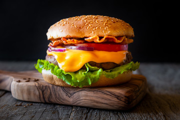 Burger with cheese, bacon, tomato and lettuce on dark wooden background